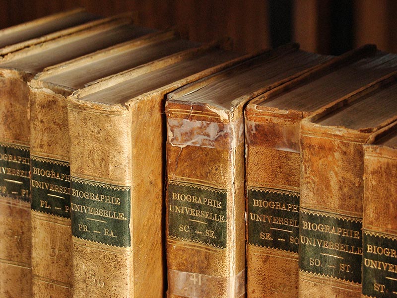 Obrázek osmi starých zaprášených encyklopedií v knihovní polici